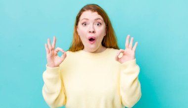 Güzel kızıl saçlı kadın şok olmuş, şaşırmış ve şaşırmış hissediyor. Onayladığını gösteriyor. İki eliyle işaret veriyor.