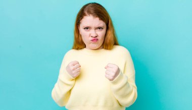 Güzel kızıl saçlı kadın kendinden emin, sinirli, güçlü ve agresif görünüyor. Yumrukları boks pozisyonunda dövüşmeye hazır.