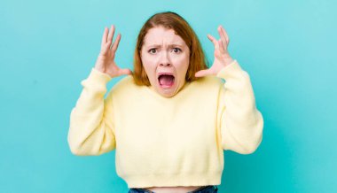 Güzel kızıl saçlı kadın ellerini havaya kaldırıp bağırıyor. Öfkeli, sinirli, stresli ve üzgün.