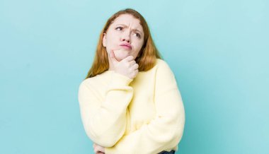 Güzel kızıl saçlı kadın düşünüyor, kuşkulu ve şaşkın hissediyor, farklı seçeneklerle, hangi kararı vereceğini merak ediyor.