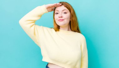 Güzel kızıl saçlı kadın saygı göstererek, onur ve vatanseverlik adına kameraya selam veriyor.