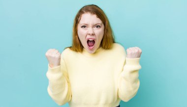 Güzel kızıl saçlı kadın sinirli bir ifadeyle bağırıyor ya da yumruklarıyla başarıyı kutluyor.