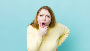 Güzel, kızıl saçlı, ağzı ve gözleri açık ve eli çenesinde olan bir kadın. Hoş olmayan bir şok geçiriyor.