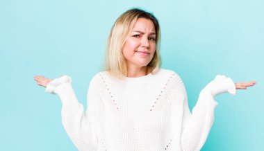 Güzel sarışın kadın şaşkın ve şaşkın hissediyor, şüpheci, farklı seçenekleri tartıyor veya komik bir ifadeyle seçiyor.