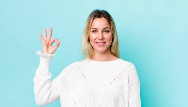 Güzel sarışın kadın mutlu, rahat ve tatmin olmuş hissediyor. Onayını iyi bir hareketle gösteriyor. Gülümsüyor.