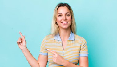 Güzel sarışın kadın mutlu bir şekilde gülümsüyor ve her iki elinde fotokopi uzayında nesne gösteriyor.