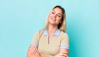 Güzel sarışın kadın kollarını kavuşturup mutlu bir şekilde gülüyor, rahat, pozitif ve tatmin edici bir pozla.