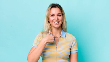 Güzel sarışın kadın mutlu, gururlu ve şaşırmış görünüyor, neşeli bir şekilde kendini gösteriyor, kendinden emin ve kibirli hissediyor.