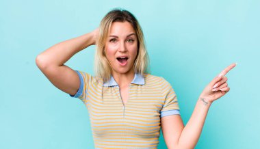 Güzel sarışın kadın gülüyor, mutlu, pozitif ve şaşırmış görünüyor, yanal fotokopi alanını işaret eden harika bir fikrin farkına varıyor.