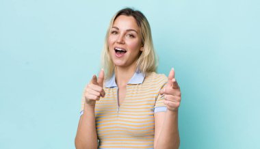 Güzel sarışın kadın, pozitif, başarılı, mutlu bir tavırla gülümsüyor kamerayı işaret ediyor, elleriyle silah işareti yapıyor.