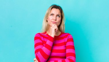 Güzel sarışın kadın düşünüyor, kuşkulu ve şaşkın hissediyor, farklı seçenekleri var, hangi kararı vereceğini merak ediyor.