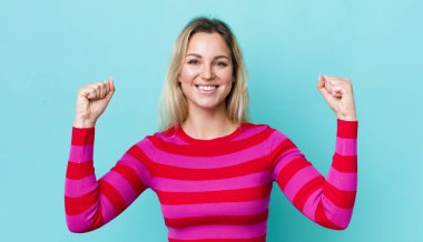 Güzel sarışın kadın mutlu, pozitif ve başarılı hissediyor, zaferi, başarıları ya da iyi şansı kutluyor.