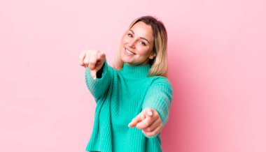 Güzel sarışın kadın mutlu ve kendinden emin hissediyor, kamerayı iki eliyle gösteriyor ve gülüyor, seni seçiyor.