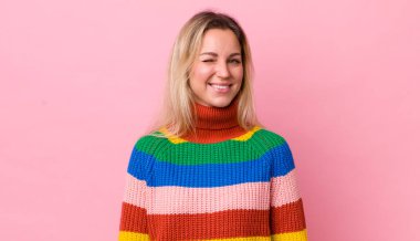 Güzel sarışın kadın mutlu ve arkadaş canlısı görünüyor, gülümsüyor ve pozitif bir tavırla sana göz kırpıyor.