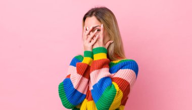 Güzel sarışın kadın korkmuş ya da utanmış hissediyor. Gözleri yarı kapalı ya da ellerle dikizliyor ya da dikizliyor.