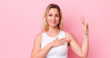 Güzel sarışın kadın mutlu, kendinden emin ve güvenilir görünüyor, gülümsüyor ve zafer işareti gösteriyor, olumlu bir tavırla.