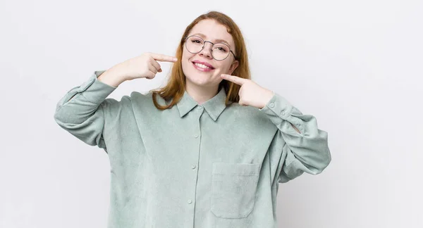 Hübsche Rote Kopffrau Lächelt Selbstbewusst Und Zeigt Auf Ihr Eigenes — Stockfoto