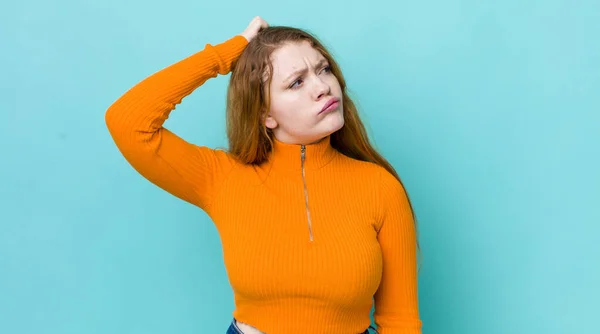 pretty red head woman feeling puzzled and confused, scratching head and looking to the side