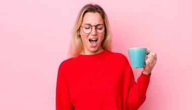 Sarışın, güzel bir kadın agresif bir şekilde bağırıyor, çok kızgın görünüyor. Kahve fincanı konsepti