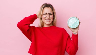 Sarışın, güzel bir kadın stresli, endişeli ya da korkmuş, elleri başının üstünde. Alarm saati kavramı