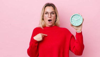 Şok olmuş ve ağzı açık, kendini gösteren sarışın, güzel bir kadın. Alarm saati kavramı