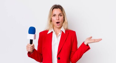 Güzel sarışın kadın şaşırmış ve şok olmuş görünüyor. Çenesi düşmüş ve elinde bir nesne var. preporter ve mikrofon kavramı