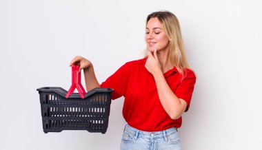 Mutlu, kendine güvenen, elleri çenesinde gülümseyen sarışın güzel kadın. Alışveriş sepeti konsepti