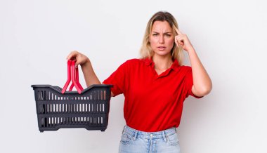 Sarışın, güzel bir kadın şaşkın ve şaşkın hissediyor, deli olduğunu gösteriyor. Alışveriş sepeti konsepti