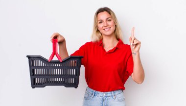 Sarışın, güzel bir kadın gülümsüyor ve arkadaş canlısı görünüyor. Bir numarayı gösteriyor. Alışveriş sepeti konsepti