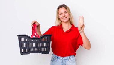 Sarışın, güzel bir kadın gülümsüyor ve arkadaş canlısı görünüyor, üç numarayı gösteriyor. Alışveriş sepeti konsepti