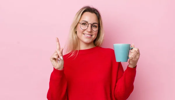ブロンドの女性は笑顔で友好的に見える1番を示してる コーヒーカップのコンセプト — ストック写真