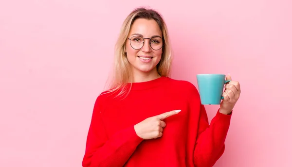 ブロンドの可愛い女は陽気に笑って幸せを感じ横を指差してる コーヒーカップのコンセプト — ストック写真