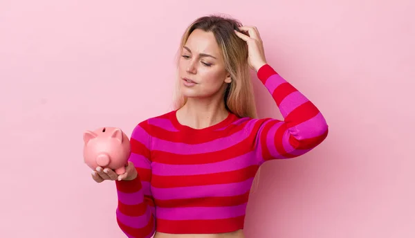 Blonde Pretty Woman Feeling Puzzled Confused Scratching Head Piggy Bank — Stockfoto