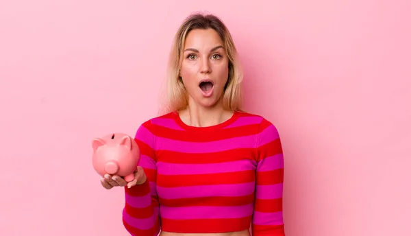 Blonde Pretty Woman Looking Very Shocked Surprised Piggy Bank Concept — Stockfoto