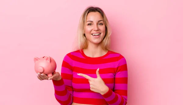 Blonde Pretty Woman Looking Excited Surprised Pointing Side Piggy Bank — Stockfoto