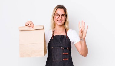 Sarışın, güzel bir kadın gülümsüyor ve arkadaş canlısı görünüyor, dört numarayı gösteriyor. teslimat paket servis kavramı