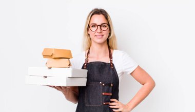 Sarışın, güzel bir kadın mutlu bir şekilde gülümsüyor, eli kalçasında ve kendinden emin. Fast food konseptini kaldır.