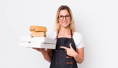 Sarışın, güzel bir kadın neşeyle gülümsüyor, mutlu hissediyor ve bir tarafı işaret ediyor. Fast food konseptini kaldır.
