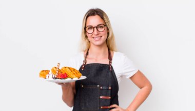 Sarışın, güzel bir kadın mutlu bir şekilde gülümsüyor, eli kalçasında ve kendinden emin. Waffle konsepti