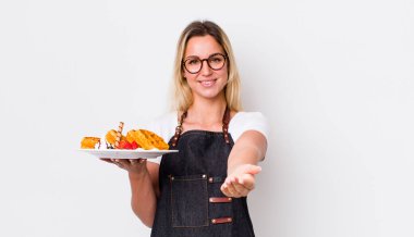 Sarışın, güzel bir kadın mutlu bir şekilde gülümsüyor ve bir konsept sunuyor. Waffle konsepti