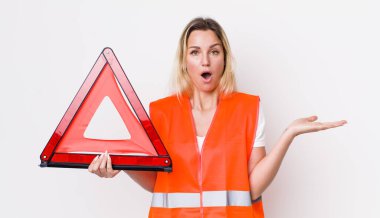 Güzel sarışın kadın şaşırmış ve şok olmuş görünüyor. Çenesi düşmüş ve elinde bir nesne var. araba üçgeni kaza konsepti