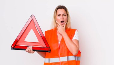 Sarışın, güzel bir kadın. Ağzı ve gözleri açık ve eli çenesinde. araba üçgeni kaza konsepti