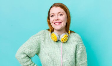 Kızıl saçlı güzel kadın mutlu bir şekilde gülümsüyor, eli kalçasında ve kendinden emin. Müzik konseptinin tadını