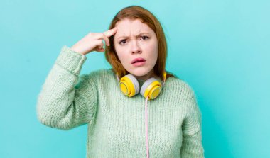 Kızıl saçlı güzel kadın kafası karışık ve şaşkın hissediyor, deli olduğunu gösteriyor. Müzik konseptinin tadını
