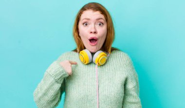 Kızıl saçlı güzel kadın şok olmuş ve ağzı açık, kendini işaret eden bir şekilde şaşırmış görünüyor. Müzik konseptinin tadını