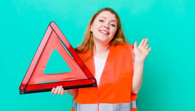 Kızıl saçlı güzel kadın mutlu bir şekilde gülümsüyor, el sallıyor, seni selamlıyor ve selamlıyor. Araba üçgeni kazası.