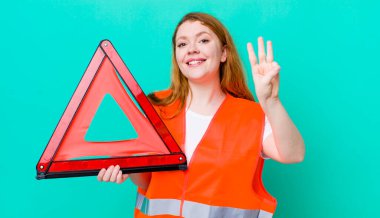 Kızıl saçlı güzel kadın gülümsüyor ve arkadaş canlısı görünüyor, üç numarayı gösteriyor. Araba üçgeni kazası.