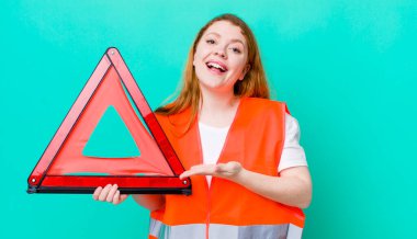 kızıl saçlı güzel bir kadın neşeli bir şekilde gülümsüyor, mutlu hissediyor ve bir konsept gösteriyor. Araba üçgeni kazası.