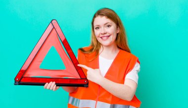 Kızıl saçlı güzel bir kadın neşeyle gülümsüyor, mutlu hissediyor ve bir tarafı işaret ediyor. Araba üçgeni kazası.