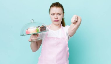 Kızıl saçlı, güzel bir kadın kendini kötü hissediyor, baş parmağını kaldırıyor. Ev yapımı kek konsepti